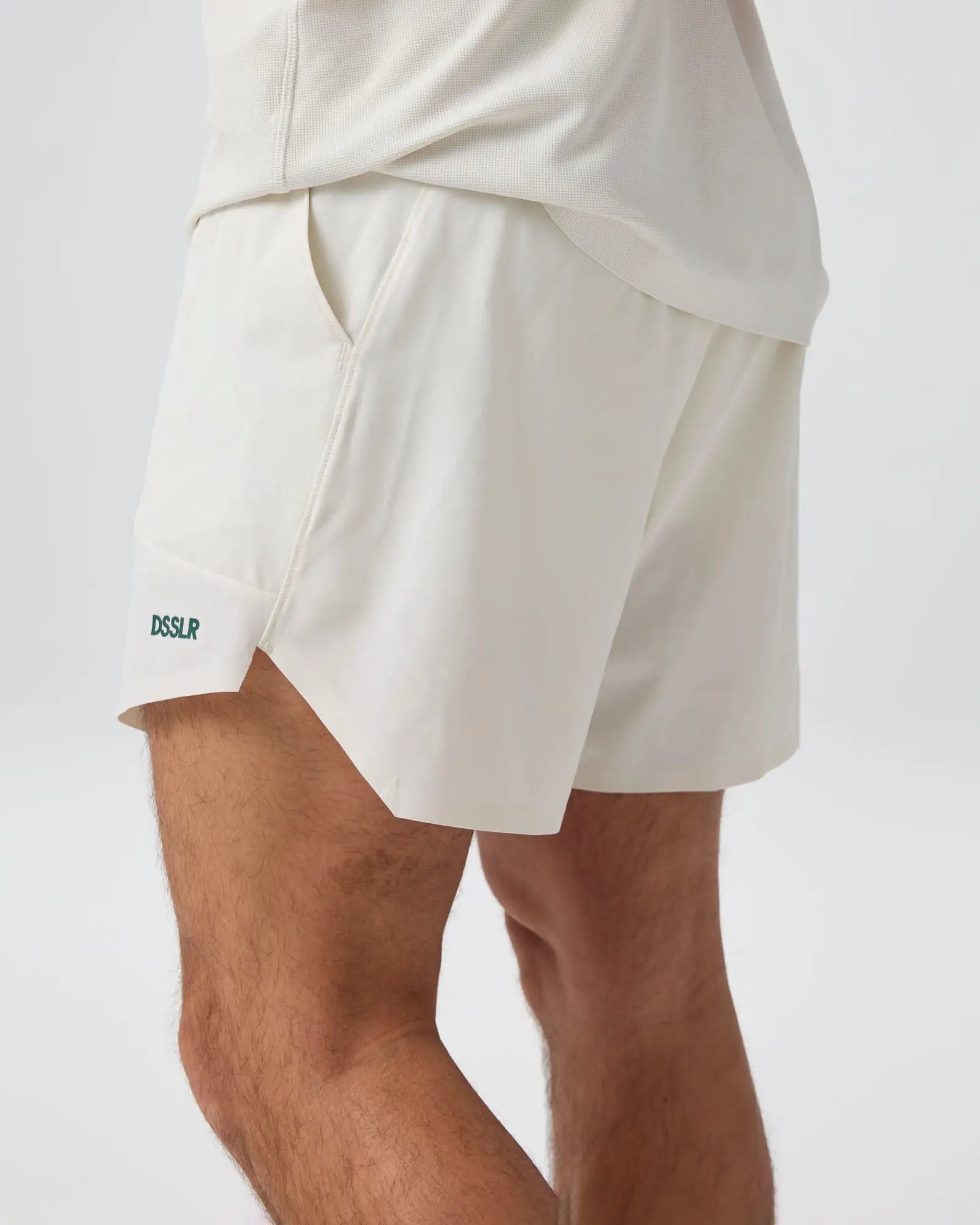 Cremeweiße Sportshorts mit einem dezent texturierten Stoff und einem kleinen grünen ’dsslr’-Logo am unteren linken Bein.