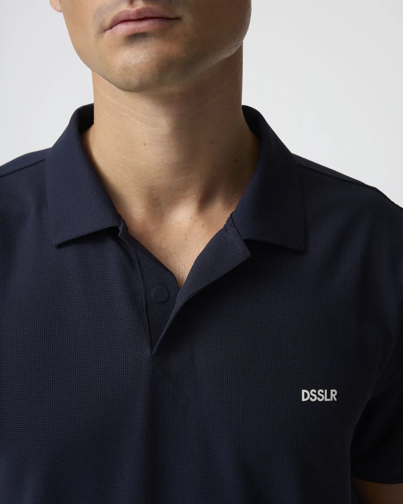 Dunkelblaues strukturiertes Poloshirt in Marineblau mit dezentem geripptem Strickmuster und weißem gesticktem ’dsslr’-Logo auf der linken Brust.