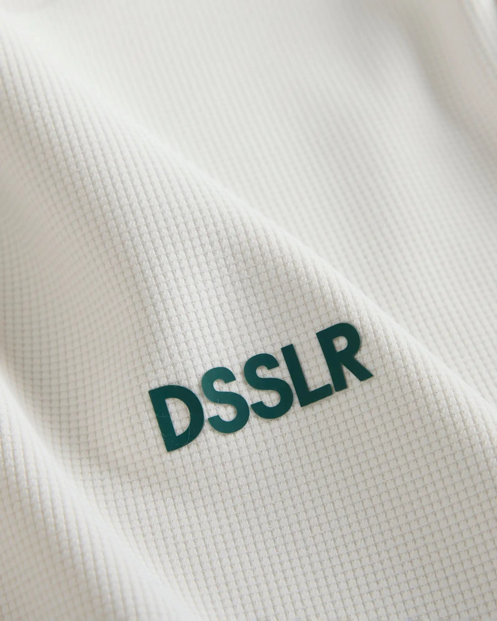 Weißer texturierter Stoff mit grünem ’dsslr’ Beschriftung, die darauf gestickt ist