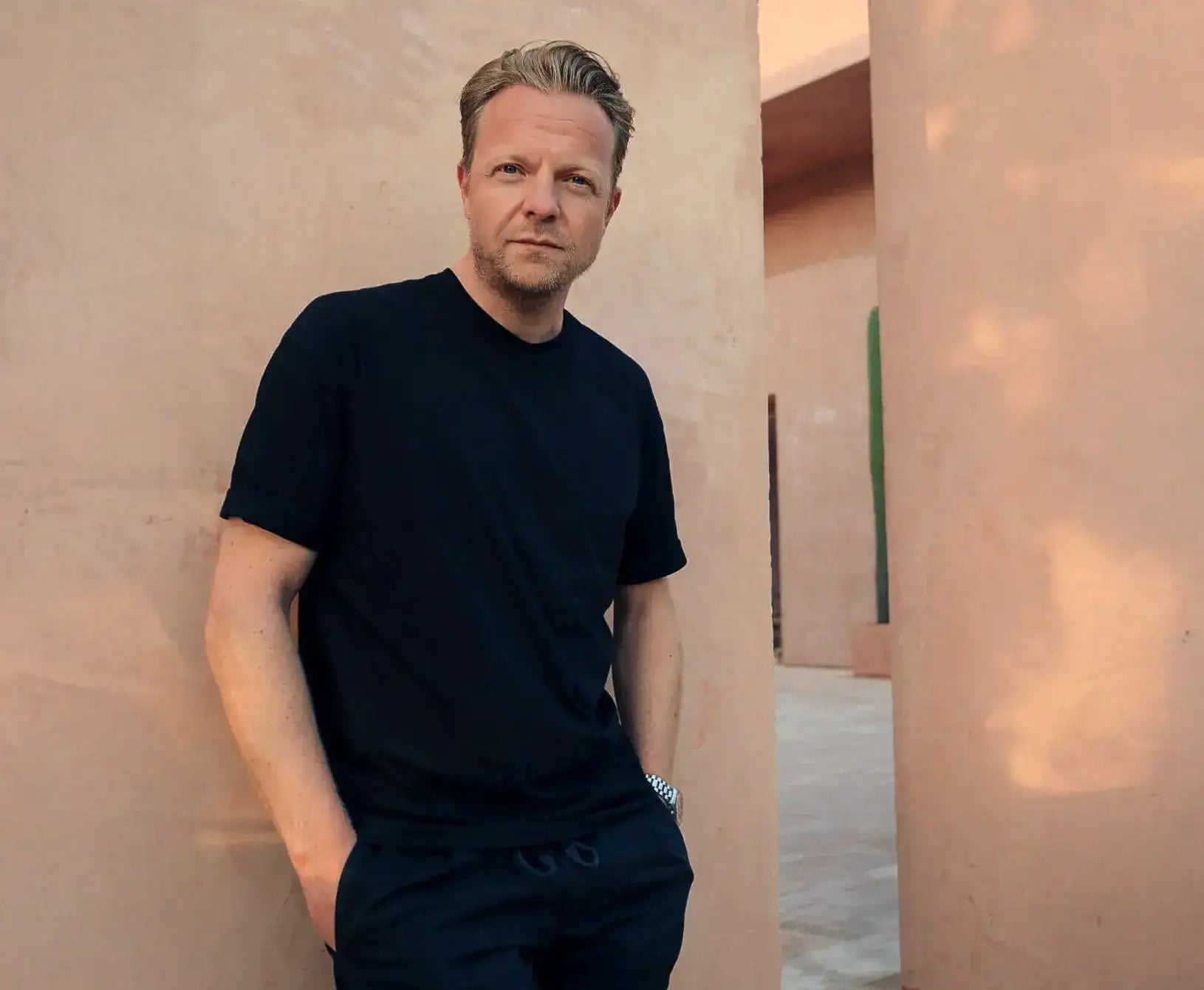 Ein Mann, der ein schwarzes kurzärmliges T-Shirt und passende dunkle Hosen trägt.